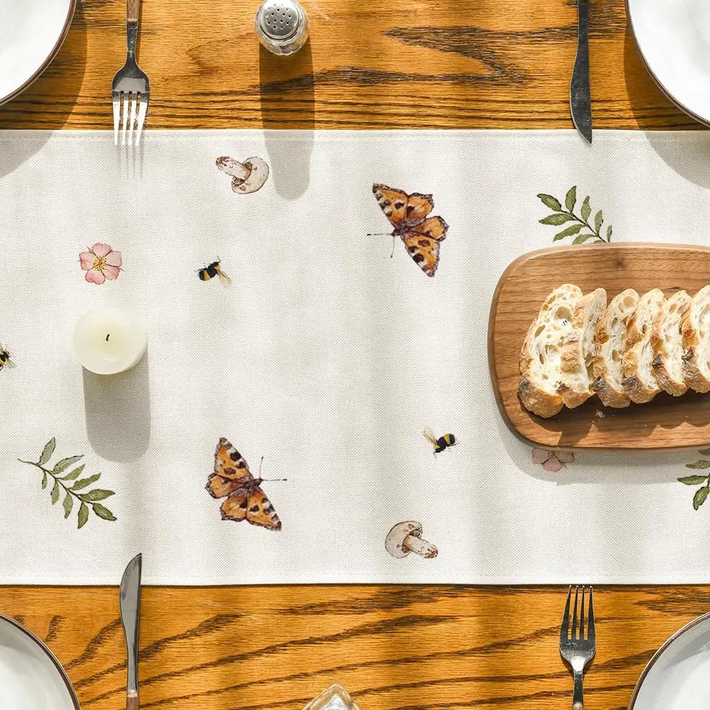 Cette image montre une table de salle à manger avec des éléments de nature tels que des papillons, des fleurs et des feuilles, ainsi qu'un plateau de pain tranché et des couverts, dans une ambiance chaleureuse et naturelle.
