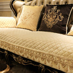 Une élégante collection de coussins et d'une courtepointe matelassée sur un canapé de style baroque ornementé avec des motifs floraux dorés.