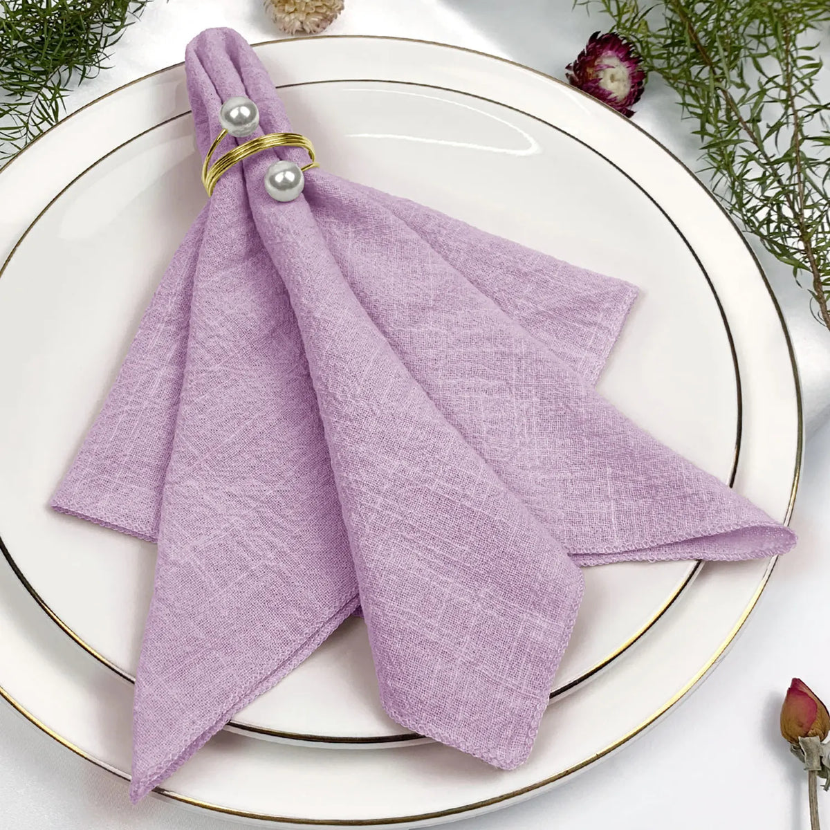 Une serviette violette pliée avec des anneaux d'or et de perles, placée sur un plat élégant avec des fleurs.