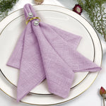 Une serviette violette pliée avec des anneaux d'or et de perles, placée sur un plat élégant avec des fleurs.