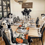 L'image montre une table de salle à manger décorée pour l'Halloween, avec des squelettes, des citrouilles et des décorations noires et blanches, créant une ambiance fantomatique et festive dans cette maison hantée.