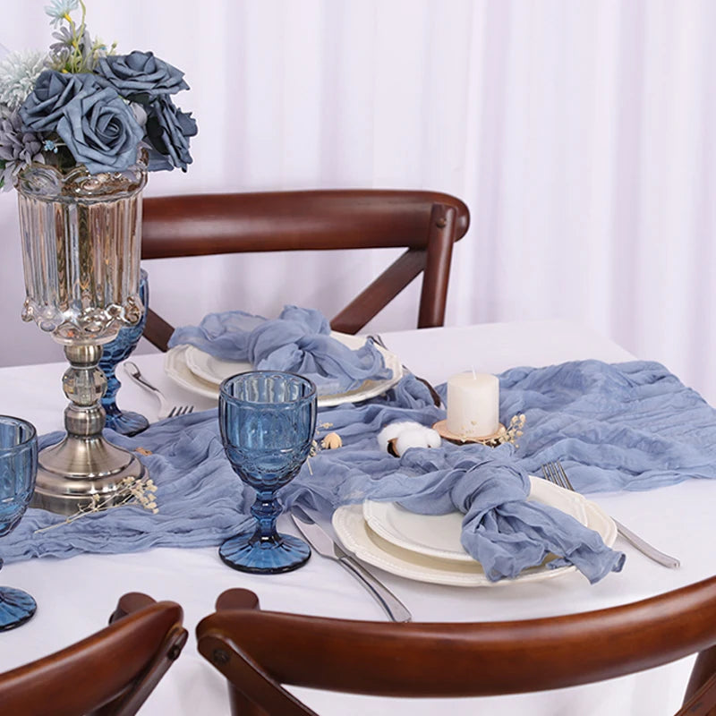 Une table de salle à manger élégante avec un centre de table floral composé de roses bleues et d'un bougeoir en argent, le tout sur un fond de rideaux blancs.