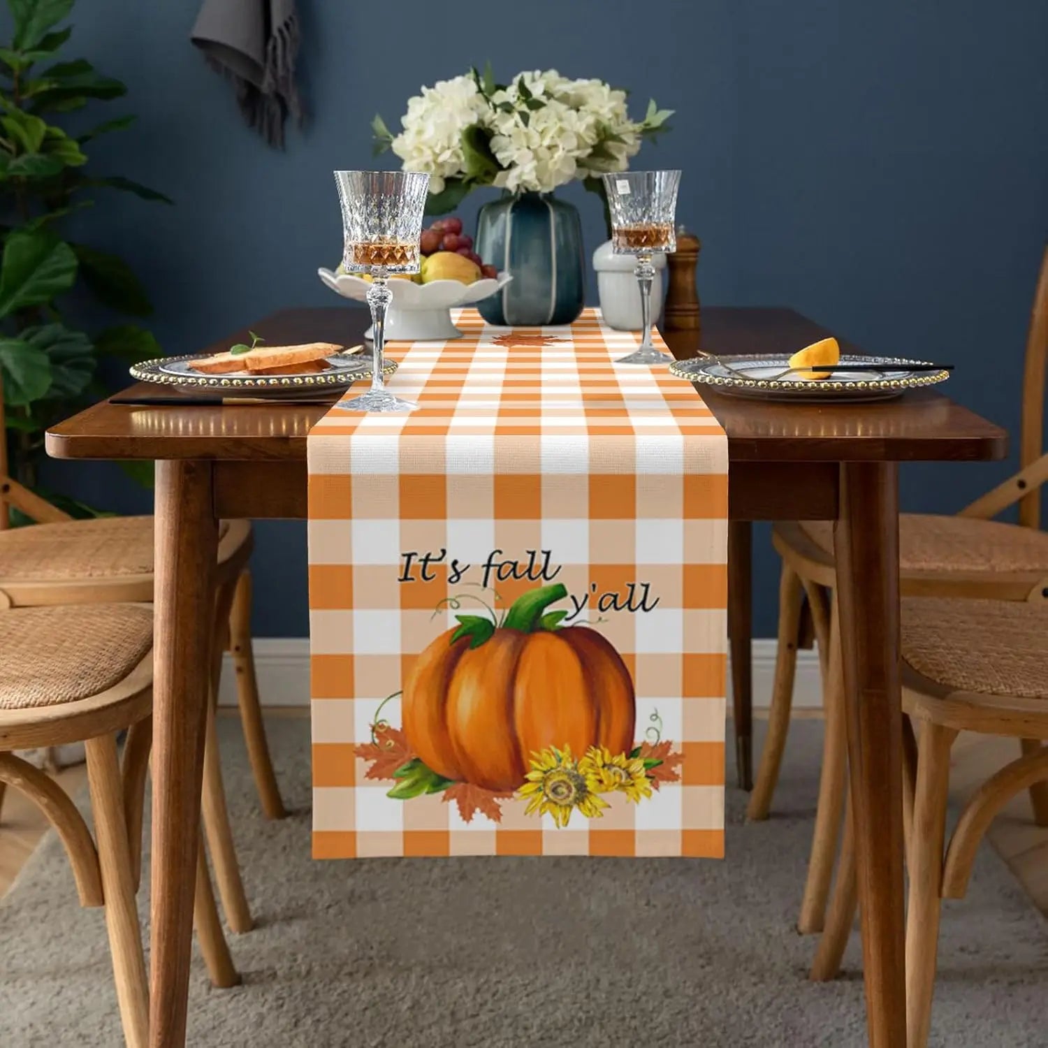 Une table élégante avec un chemin de table à carreaux orange et blanc, une décoration florale, des verres et des fruits, créant une ambiance conviviale et chaleureuse pour la saison automnale.