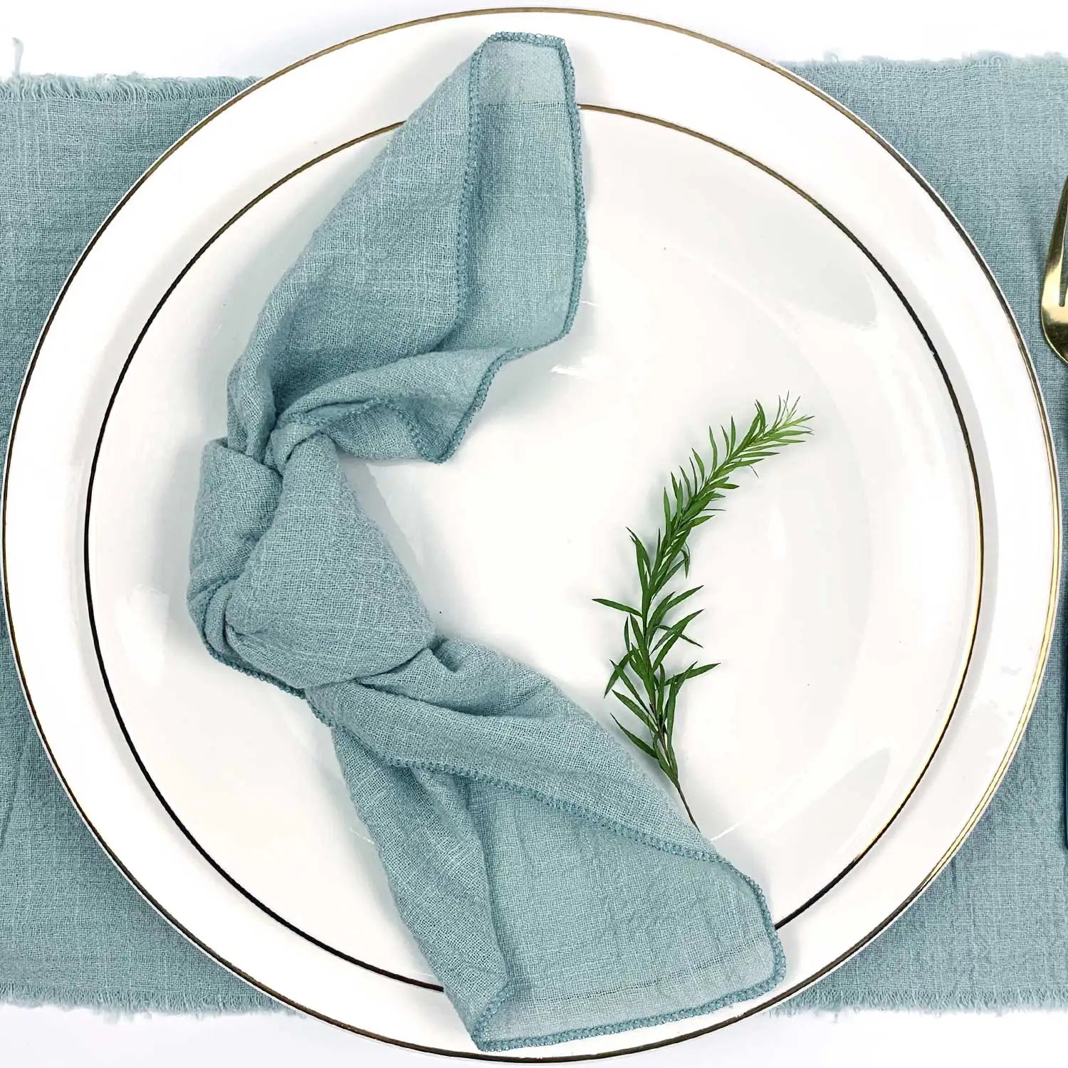 Une serviette de table gris-vert nouée sur une assiette blanche avec une branche de romarin.