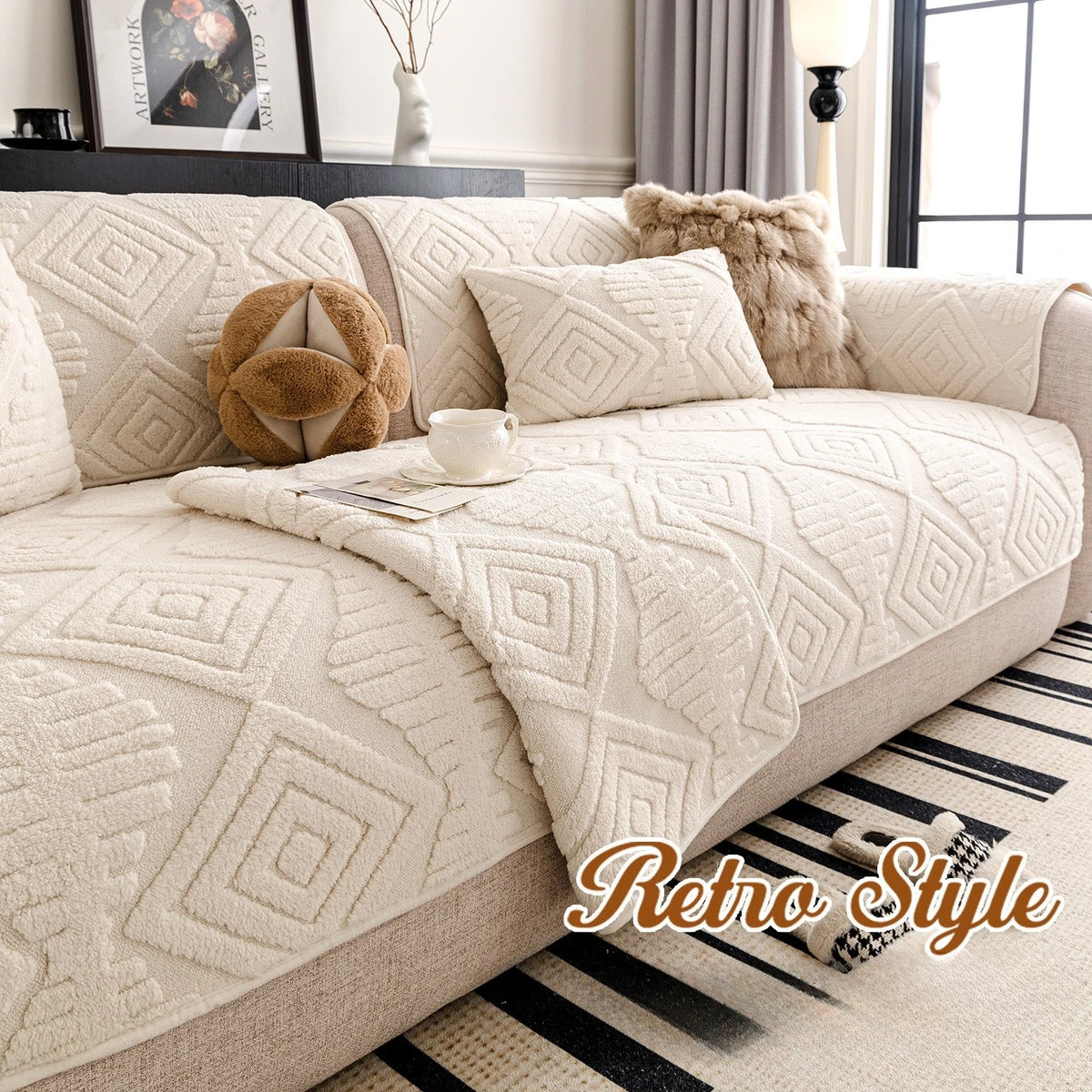 L'image montre un canapé confortable et douillet recouvert d'un plaid aux motifs géométriques beiges, accompagné de coussins décoratifs et d'un vase avec des branches, dans un décor de style rétro.