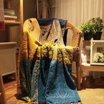 Coussin moelleux et coloré avec un motif bohème, aux tons chauds jaunes et bleus, reposant dans un fauteuil en rotin.