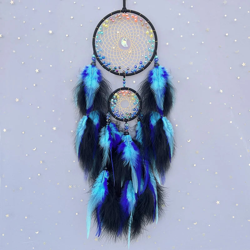 Rêve capteur suspendu en plumes noires et bleues avec des éléments décoratifs en perles et pierres colorées sur un fond de ciel étoilé.