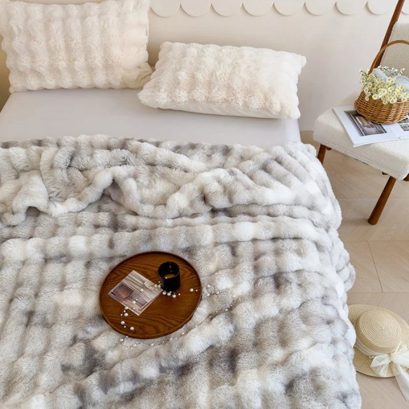 Décor cosy et douillet avec une couverture moelleuse et des coussins en peluche blanche, posés sur un plateau en bois avec des accessoires décoratifs, dans un environnement chaleureux et accueillant.