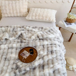 Décor cosy et douillet avec une couverture moelleuse et des coussins en peluche blanche, posés sur un plateau en bois avec des accessoires décoratifs, dans un environnement chaleureux et accueillant.