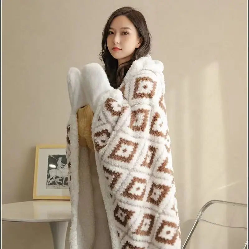 Une femme aux cheveux longs et bruns porte une couverture blanche et beige ornée de motifs géométriques chauds et accueillants.