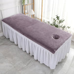 Une table de massage confortable avec une surface recouverte de tissu violet et une jupe blanche élégante.