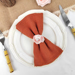 Une élégante table de dîner avec une assiette blanche ornée d'une serviette en lin terracotta nouée d'une rose rose.