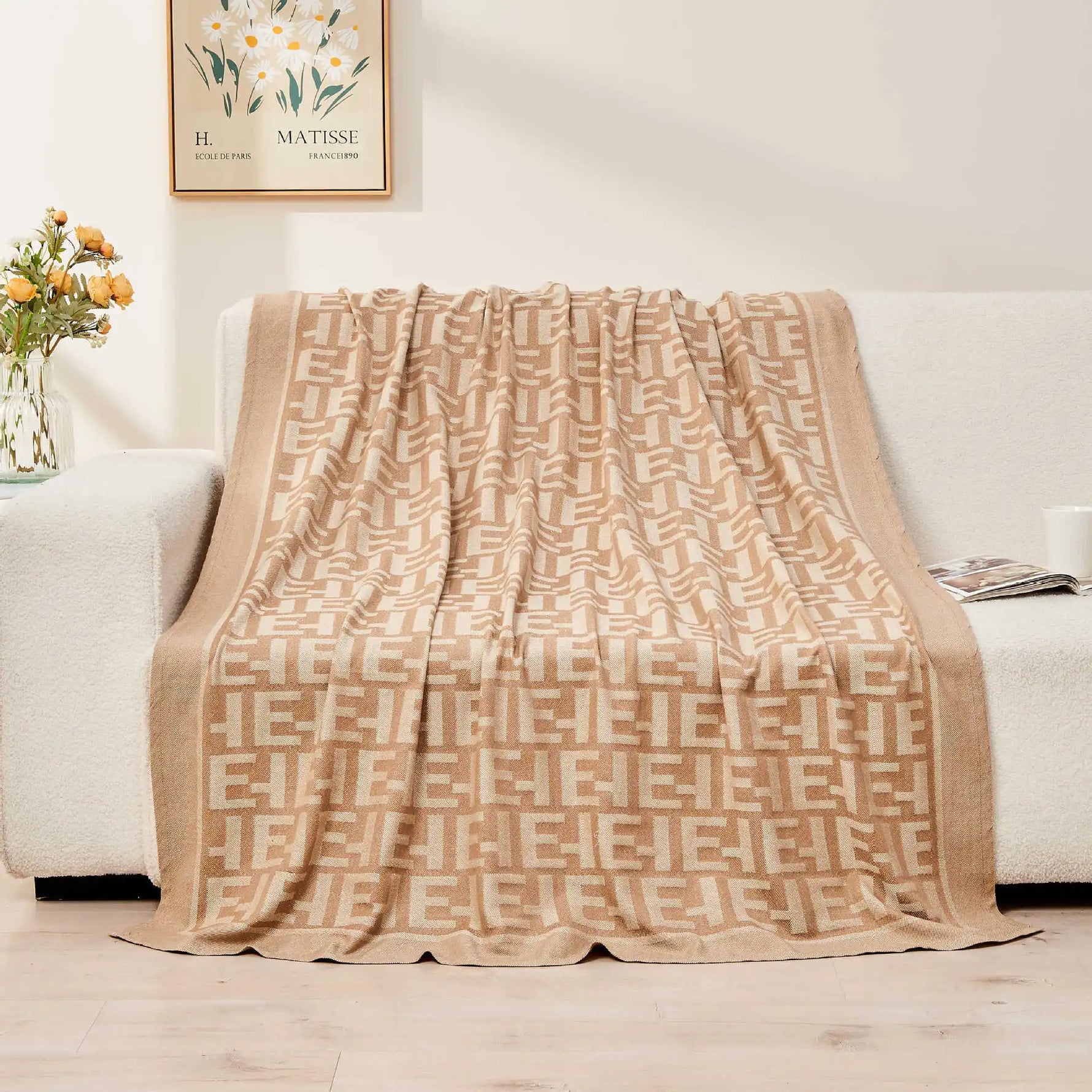 Couverture beige avec un motif géométrique élégant sur un canapé confortable, accompagnée d'une affiche Matisse et d'un vase avec des fleurs, créant une ambiance chaleureuse et design dans cette pièce.