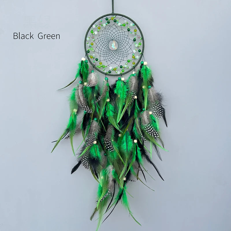 Un magnifique attrape-rêves noir et vert orné de plumes multicolores et de perles, suspendu sur un fond gris clair.