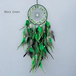 Un magnifique attrape-rêves noir et vert orné de plumes multicolores et de perles, suspendu sur un fond gris clair.