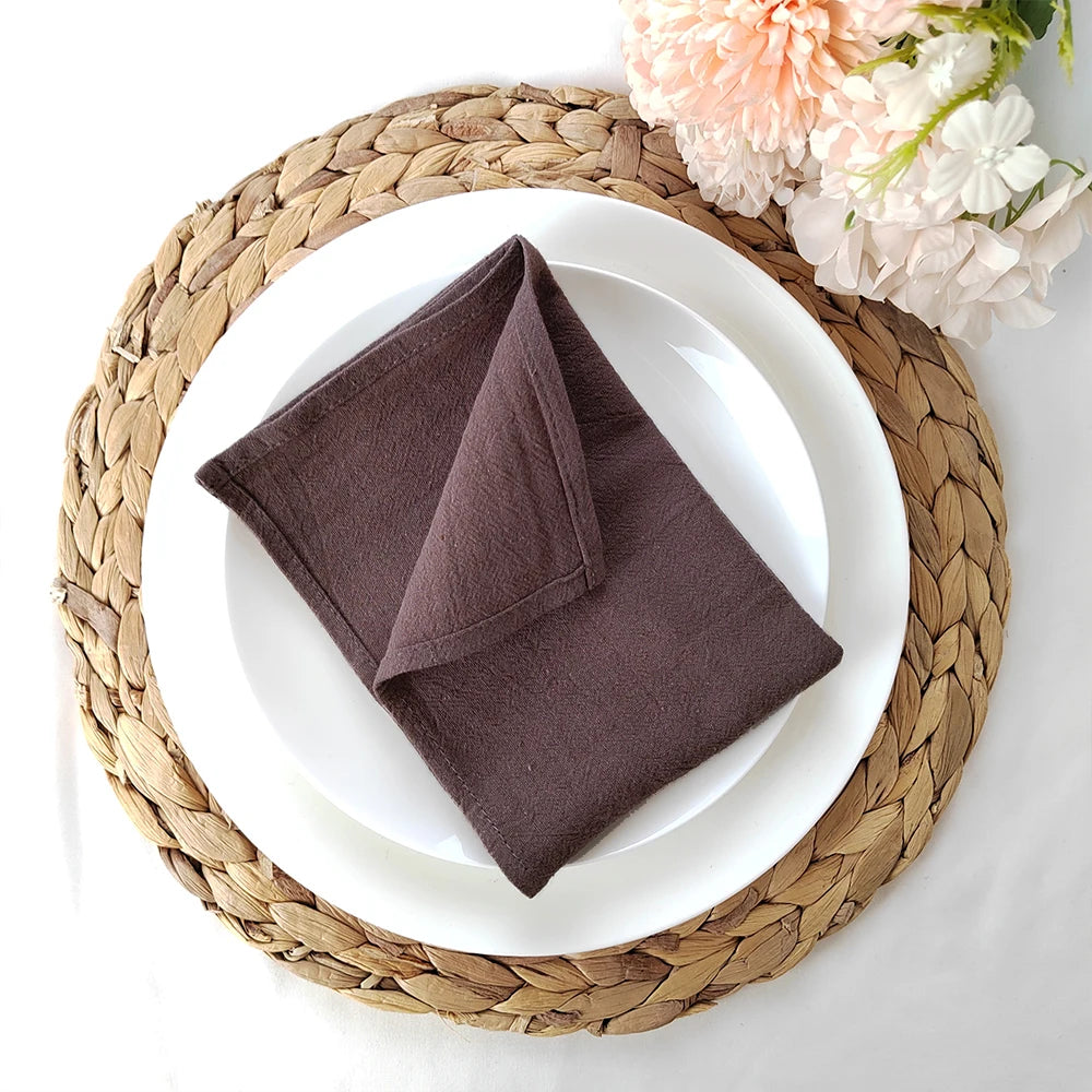 Serviette de table pliée sur une assiette blanche posée sur un set de table en osier tressé, entourée de fleurs rose et blanche.