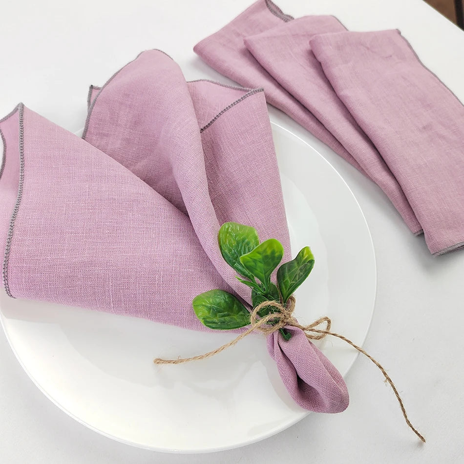 Des serviettes de table de couleur rose pastel soigneusement pliées sur une assiette blanche, décorées d'un bouquet de feuilles vertes attachées avec une ficelle.