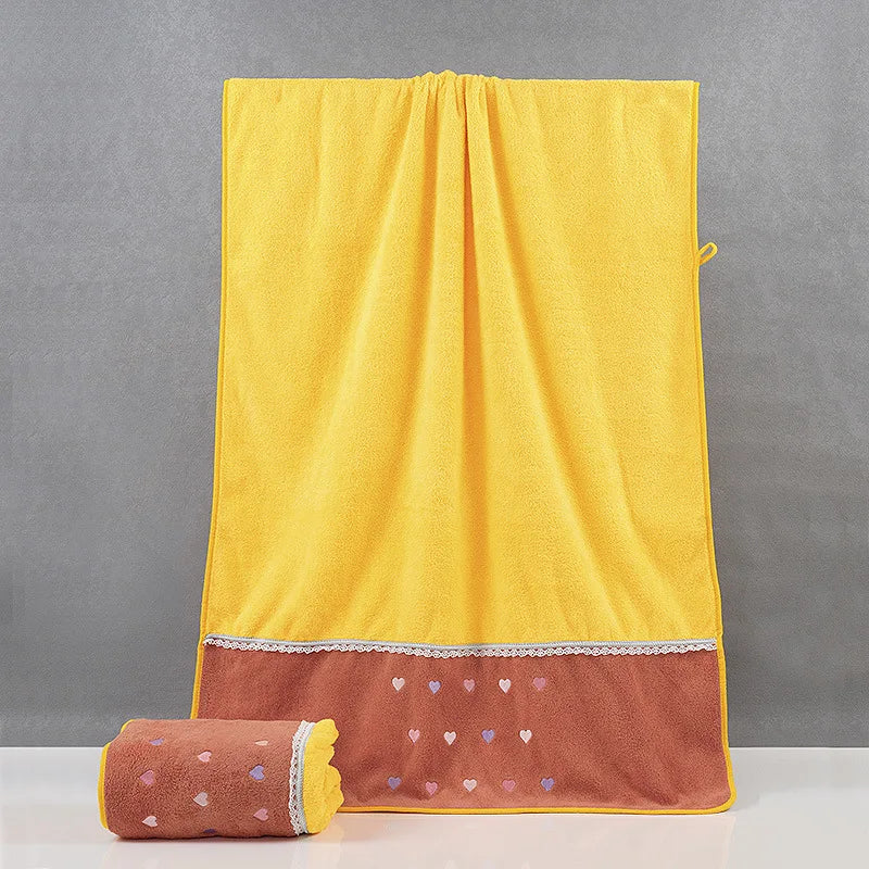 Couverture jaune moelleuse ornée de cœurs colorés sur le bas, posée sur un sol gris.