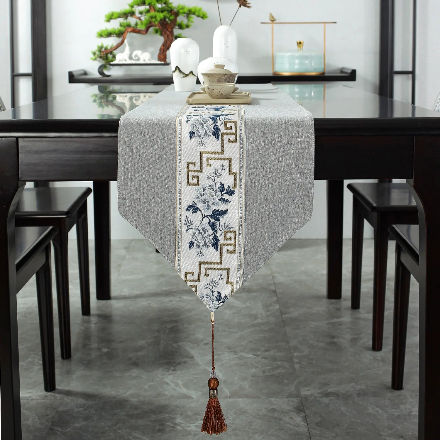 Un chemin de table décoratif orné de motifs floraux et géométriques, posé sur une table en bois avec des éléments de décoration asiatiques.