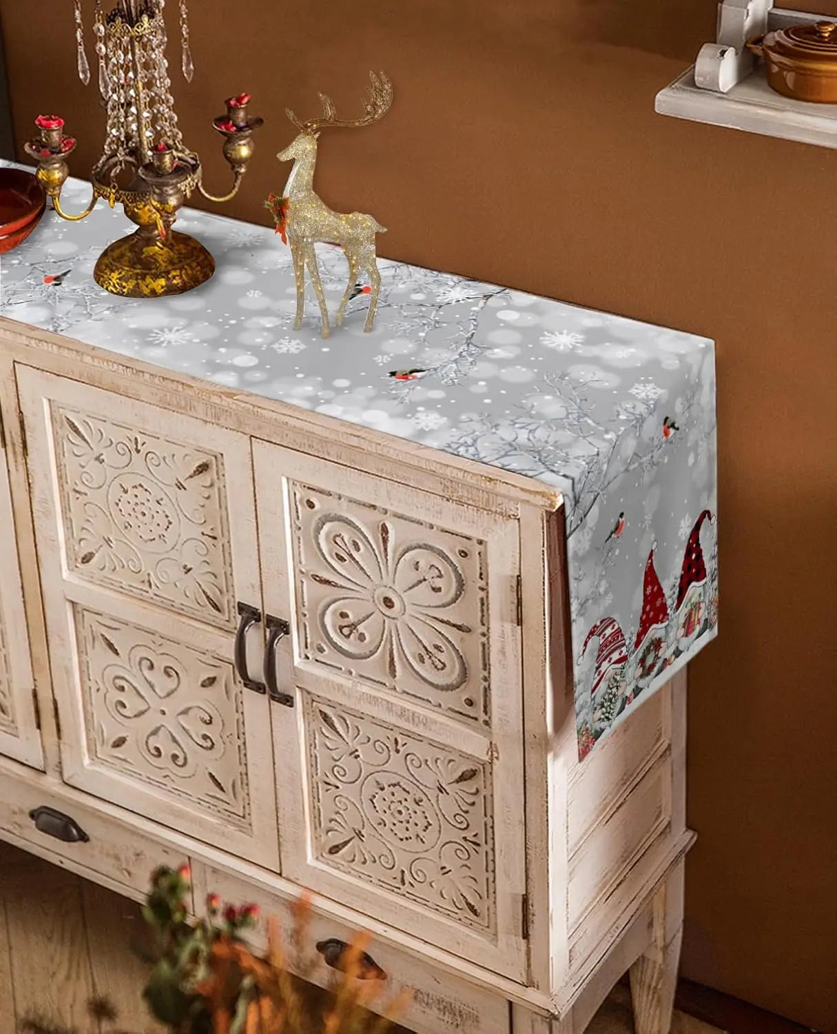 Meuble blanc vintage avec des motifs ornementaux, supportant des objets décoratifs dorés et des figurines de renne pour créer une ambiance de Noël.