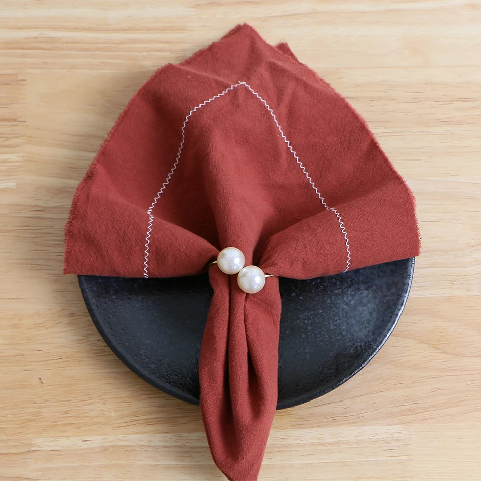 Un élégant nœud en tissu rouge avec deux perles décore une coupelle de forme ronde sur un fond en bois.