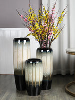 Vase en céramique noir et blanc avec bouquet de branches à fleurs jaunes et roses.