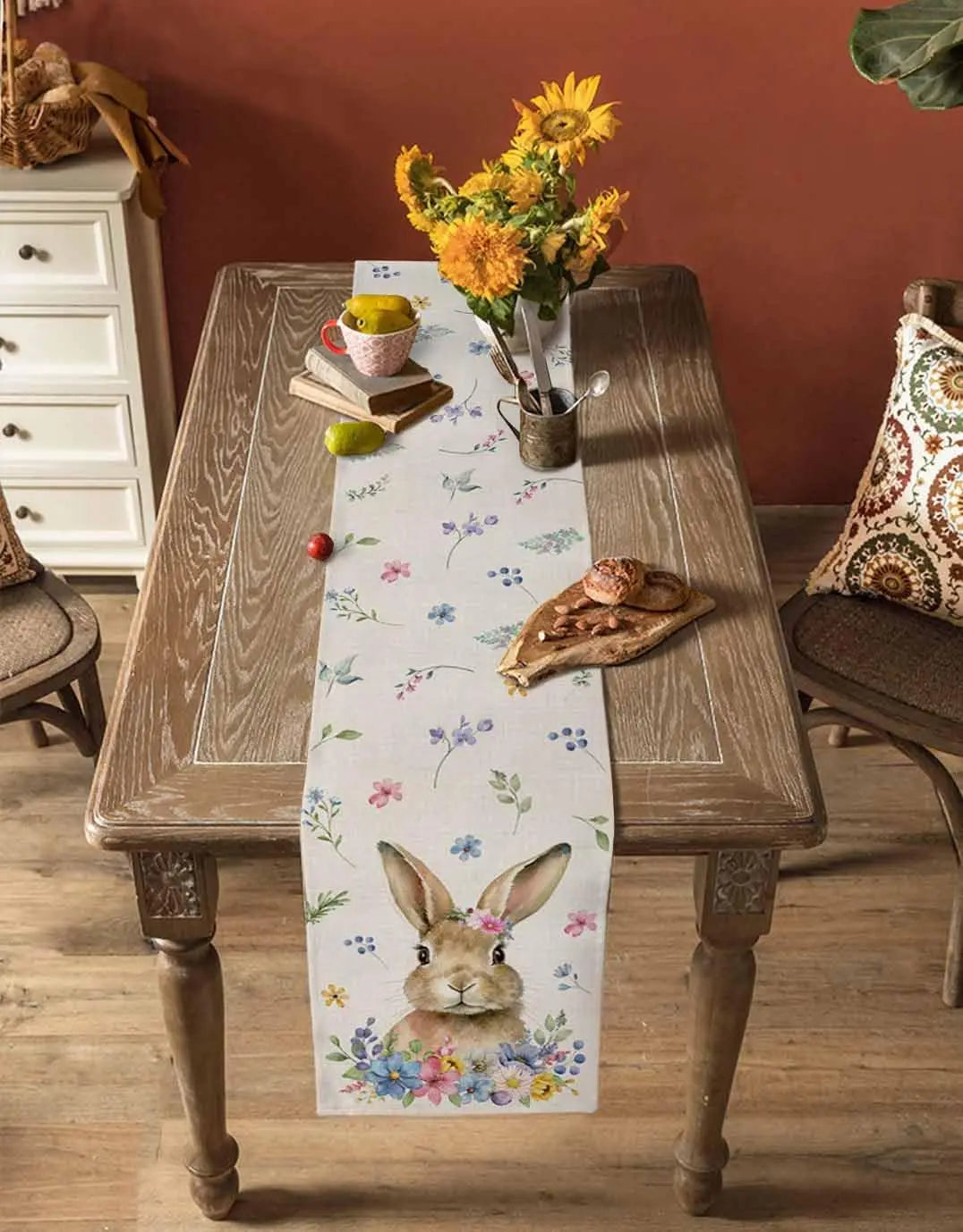 Décoration printanière rustique avec bouquet de fleurs jaunes, tasse de thé et livre posés sur une table en bois aux pieds ouvragés, avec un chemin de table fleuri mettant en scène un lapin.