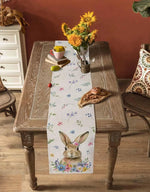 Décoration printanière rustique avec bouquet de fleurs jaunes, tasse de thé et livre posés sur une table en bois aux pieds ouvragés, avec un chemin de table fleuri mettant en scène un lapin.