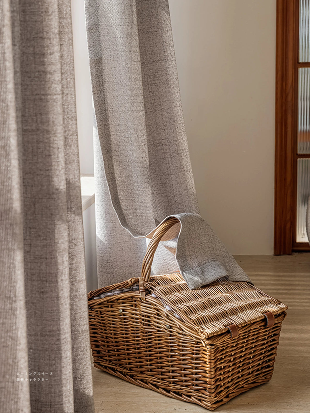 Voilage occultant gris clair tombant au sol à côté d'un panier en osier.