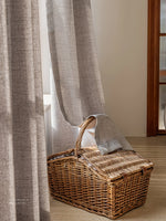 Voilage occultant gris clair tombant au sol à côté d'un panier en osier.