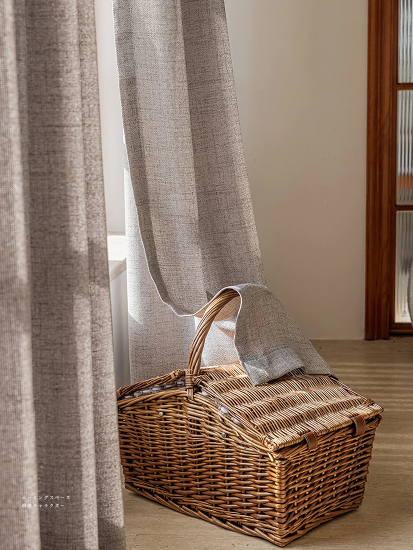 Voilage occultant gris clair tombant au sol à côté d'un panier en osier.