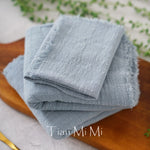 Une serviette grise douce et texturée, empilée sur une surface en bois avec un décor végétal en arrière-plan.