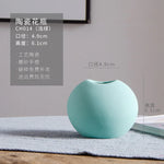 Vase en céramique de forme ronde en couleur verte pastel, posé sur un tapis gris dans un intérieur moderne.