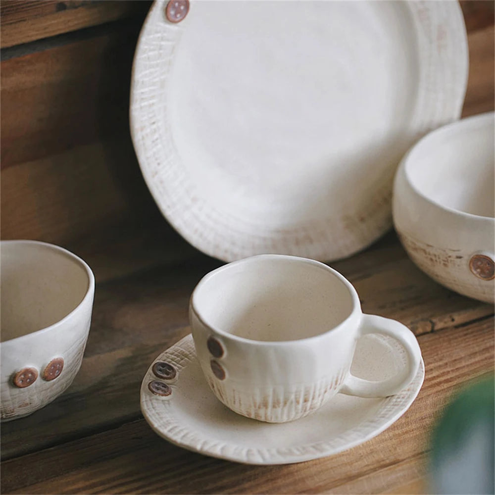 Des tasses et une assiette en céramique blanche décorées de boutons sur une surface en bois.