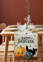 La table est joliment décorée pour la fête d'Halloween, avec des citrouilles décoratives, un chat noir et une bannière "Happy Halloween" sur un chemin de table festif.