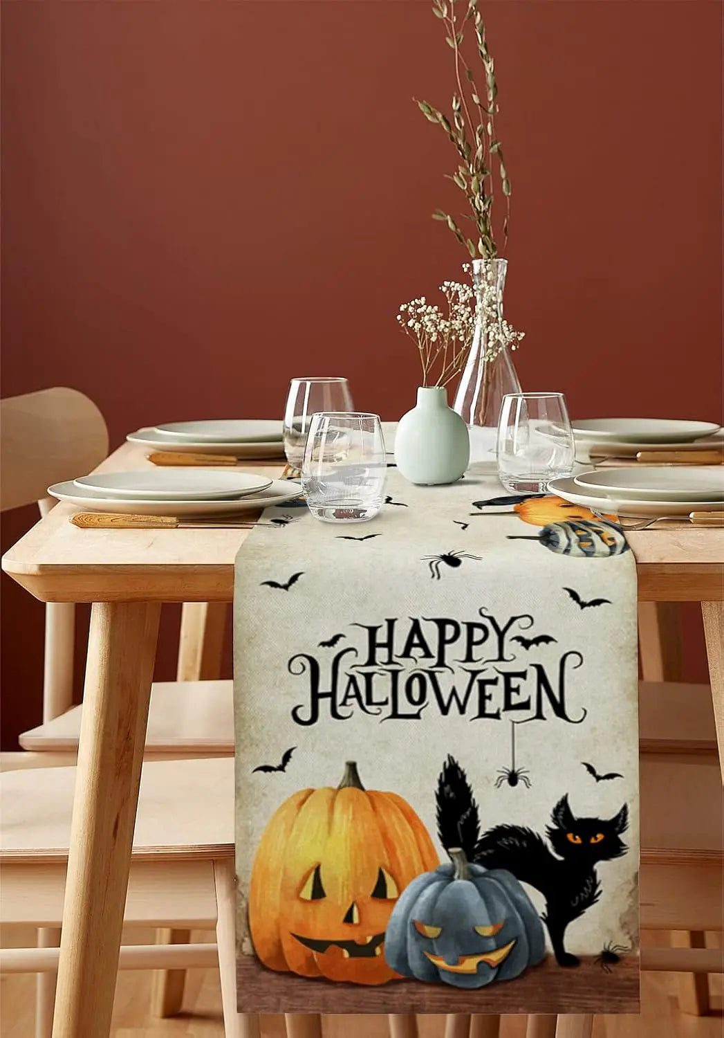 La table est joliment décorée pour la fête d'Halloween, avec des citrouilles décoratives, un chat noir et une bannière "Happy Halloween" sur un chemin de table festif.