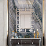 Une console élégante ornée de décorations dorées et d'un miroir géométrique est placée devant un mur de marbre gris, créant une atmosphère luxueuse et raffinée.
