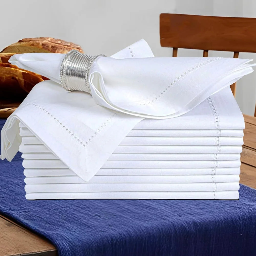 Pile de serviettes de table blanches sur une nappe bleue, avec un beau bracelet argenté et des viennoiseries sur le côté.