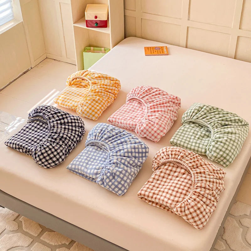 Ensemble de draps et taies d'oreiller colorés et à carreaux, offrant un choix varié de motifs et de tons pastel dans une chambre.