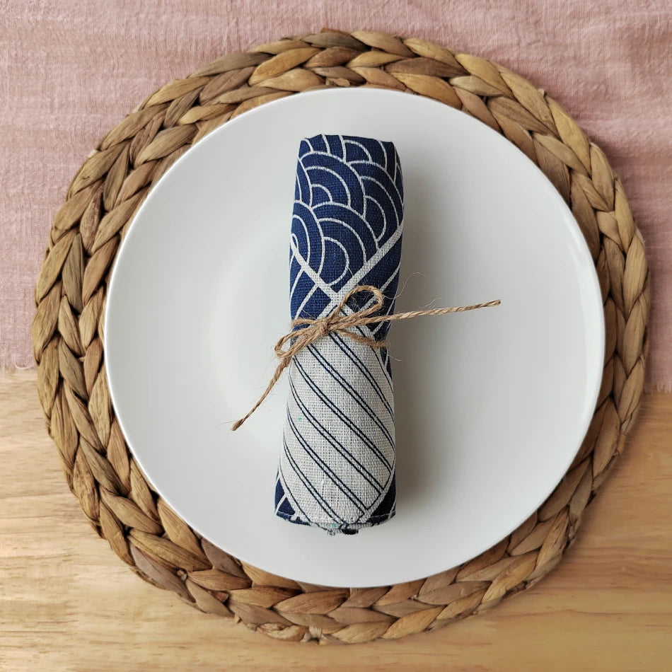 Un rouleau de serviette enroulé dans un motif bleu et blanc, attaché avec une corde, posé sur un tapis tressé en osier.