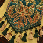 Riche tapisserie aux motifs floraux colorés ornée de pompons et de glands, évoquant un style artisanal traditionnel.