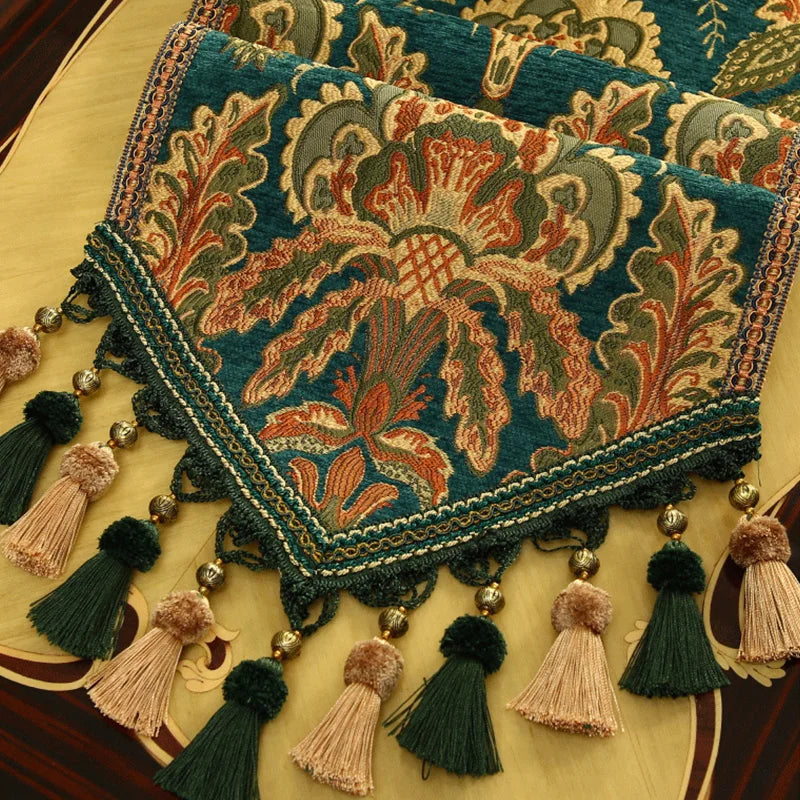 Riche tapisserie aux motifs floraux colorés ornée de pompons et de glands, évoquant un style artisanal traditionnel.