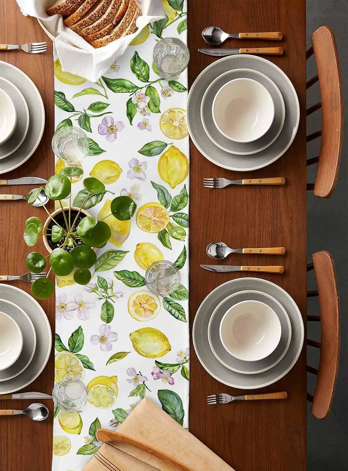 La table est joliment décorée avec des assiettes, des couverts et un chemin de table aux motifs citrons, limes et feuilles vertes, créant une atmosphère fraîche et accueillante pour un repas.