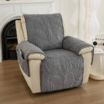 Un fauteuil confortable recouvert d'un motif de feuilles gris, placé dans un salon lumineux avec une cheminée.