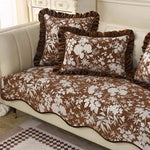 Coussins et dessus de lit décoratifs à motifs floraux bruns et blancs, créant une ambiance chaleureuse et confortable dans cette pièce.