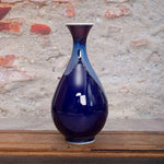 Un vase en céramique bleu foncé avec des nuances de bleu plus claires, posé sur un vieux sol en bois.