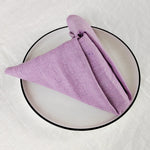 Une serviette de cuisine en lin de couleur mauve posée sur un plateau circulaire noir.