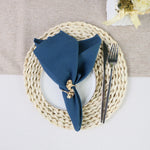Un élégant ensemble de table composé d'un napperon tressé beige, d'une assiette blanche et d'une serviette de table bleu marine décorée d'un élément doré.