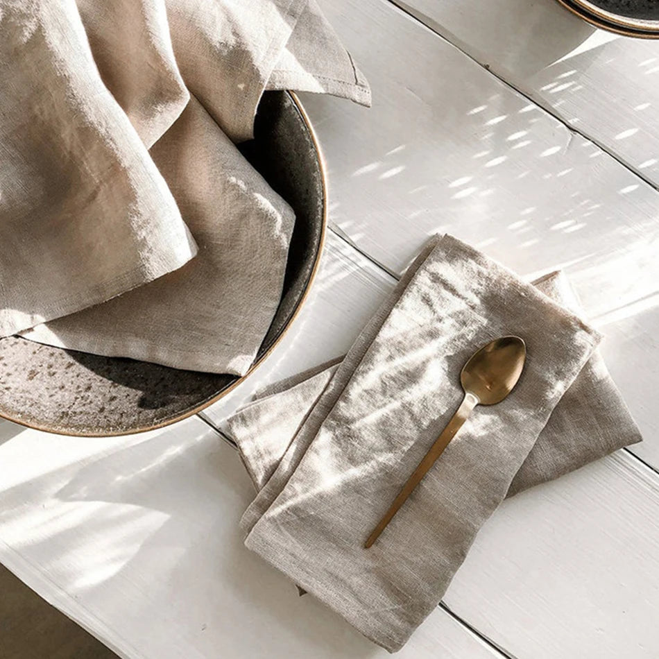 La photo montre un service de table avec une assiette en céramique, un linge de table texturé et une cuillère dorée, créant une ambiance élégante et épurée.