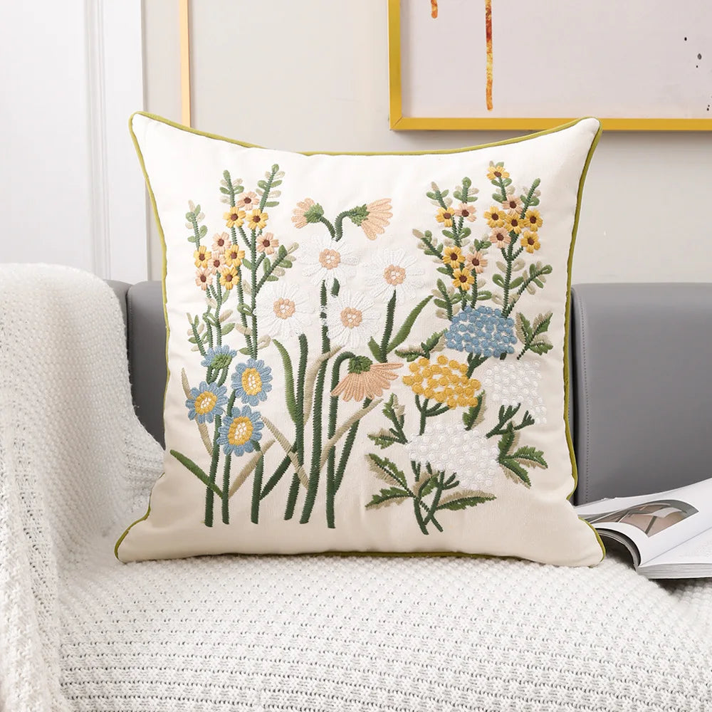 Un coussin décoratif aux motifs floraux variés avec des fleurs jaunes, blanches et bleues sur un fond blanc.